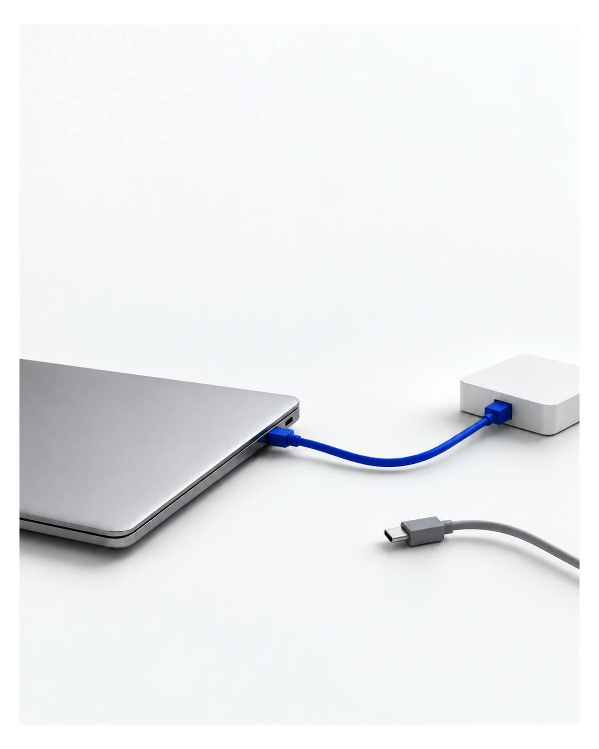 A laptop connects to a white hub by a blue cable while a separate grey cable remains unplugged